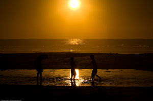 Three_children_play_in_a_lagoon_formed_from_high_tide_on_Morro_Strand_State_Beach_at_sunset